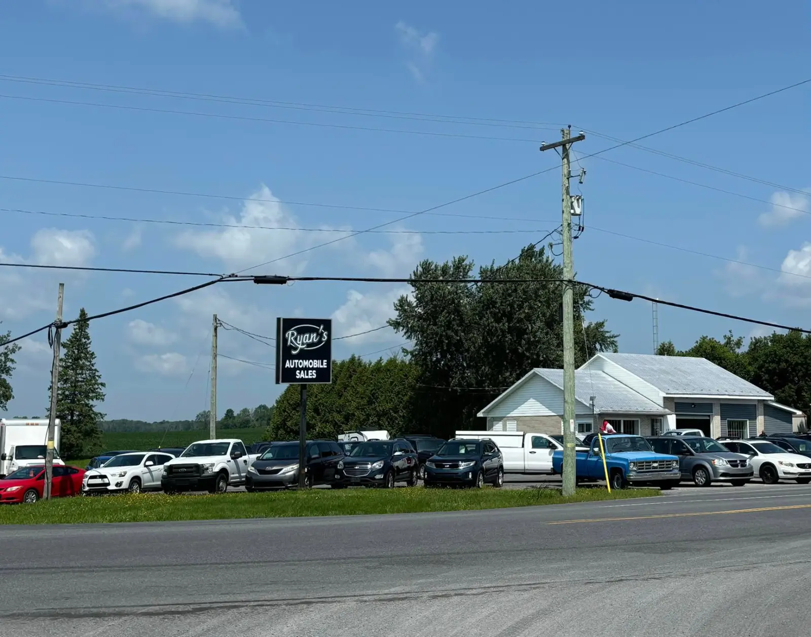 Ryan's Auto Sales lot, roadside sign and white building in Maxville, Ontario